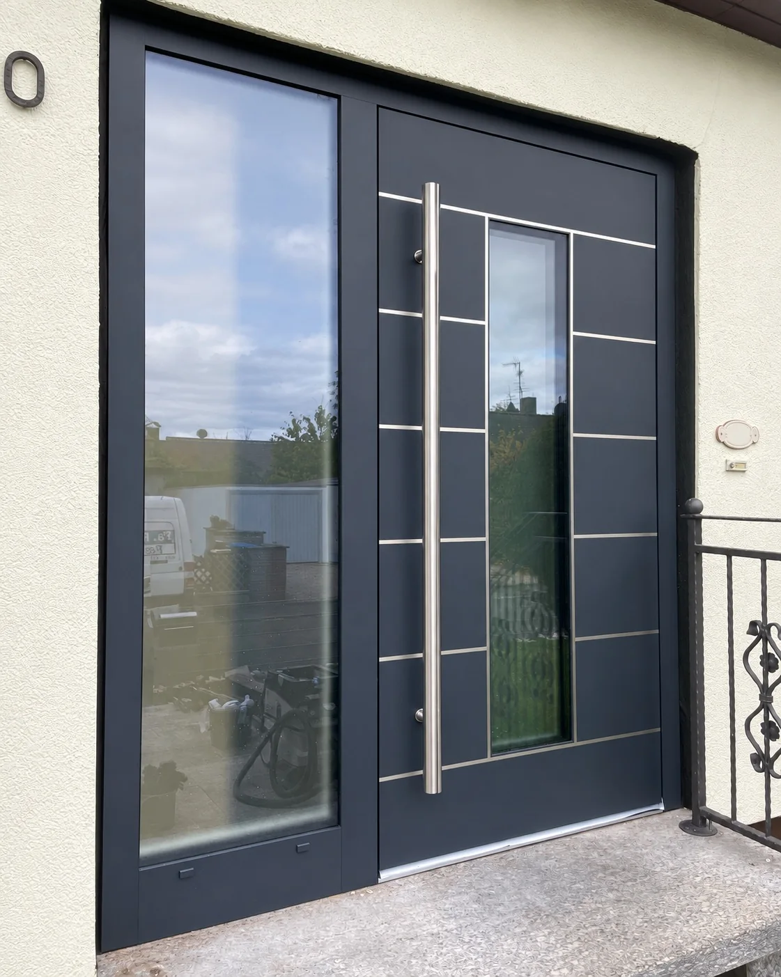 Dunkle Haustür mit verglastem Seitenteil und langem Edelstahlgriff